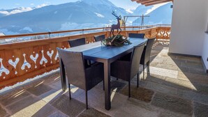 A balcony with a table and chairs, a decorative deer, and a mountain view. - Ski Apartment with panoramic views (Mittersill)