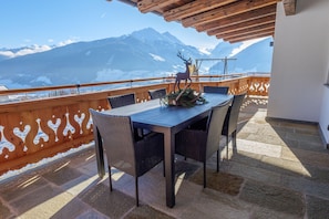 Ein Balkon mit Tisch und Stühlen, einer Dekoration mit Hirschmotiv und Blick auf die Berge.