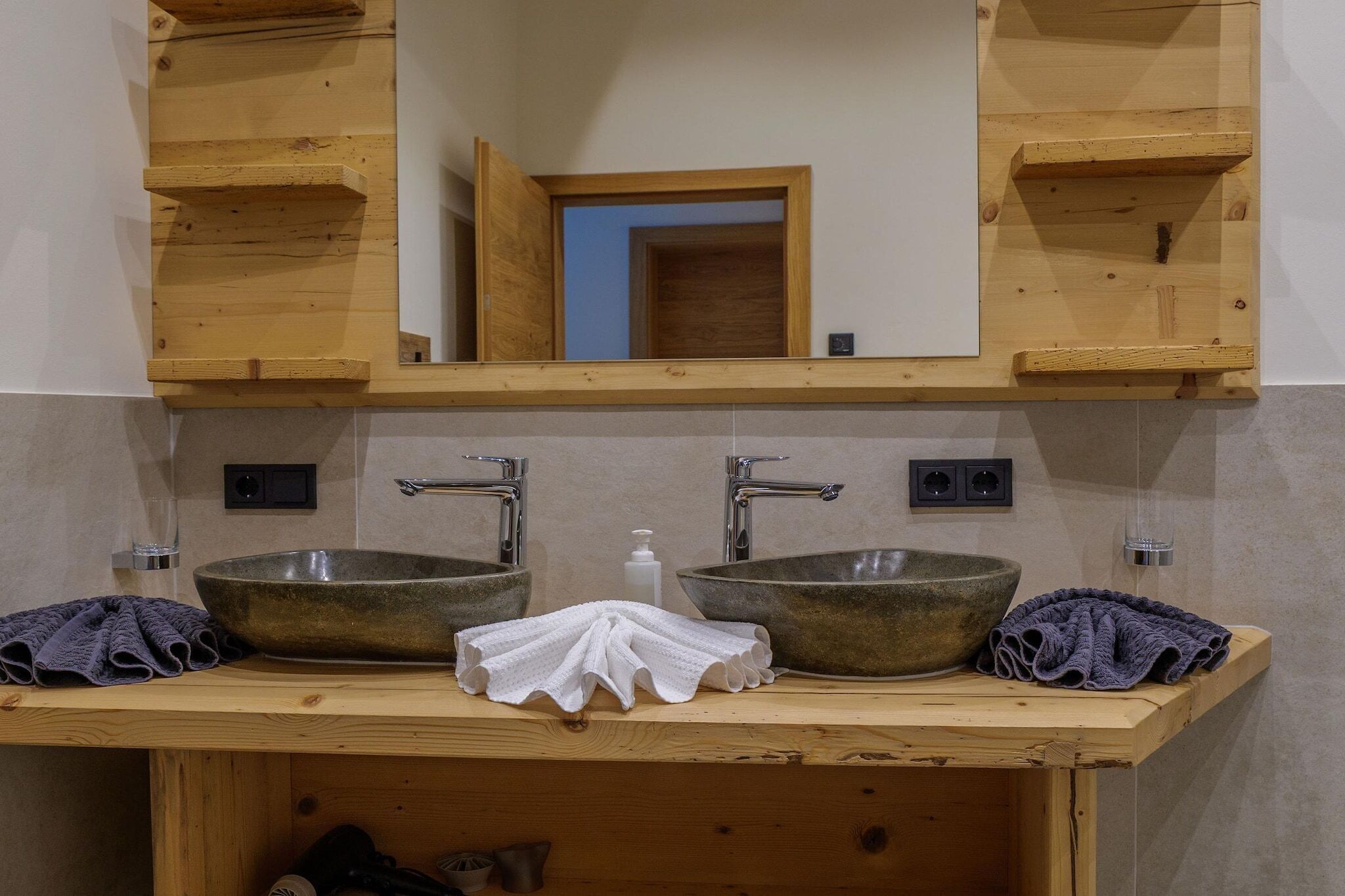 A bathroom with two sinks, wooden shelves, a mirror, and a towel rack.