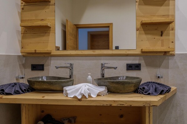 Ein Badezimmer mit zwei Waschbecken, Holzregalen, einem Spiegel und einem Handtuchhalter.