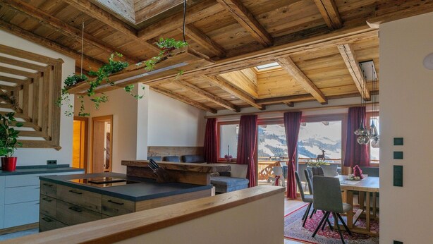 A modern kitchen with wooden beams, a dining area with a table and chairs, and a view of mountains through large windows. - Ski Apartment with panoramic views (Mittersill)