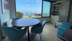 A room with a large window, a round table with chairs, a bookshelf, and a bed. - Port Saplaya Apartment (Alboraya)
