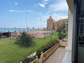 A balcony with a view of a beach, a tennis court, and a multi-story building.