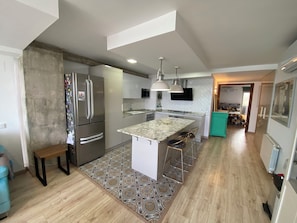 A modern kitchen with a central island, stainless steel appliances, pendant lighting, and a patterned rug.