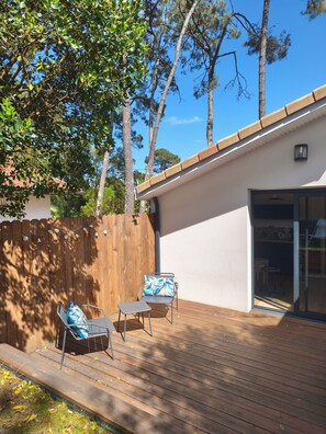 Um pátio com duas cadeiras e uma mesa, um deck de madeira, e um edifício branco com porta de vidro.
