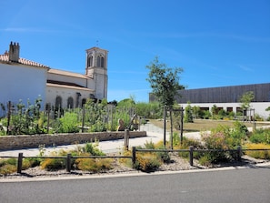 A courtyard with a stone wall, a pathway, and a building with a clock tower. - Bois Marin - Pool & Beach 500 meters away (Bretignolles-sur-Mer)