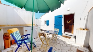 Un patio con una mesa, sillas, un paraguas verde y una puerta azul.