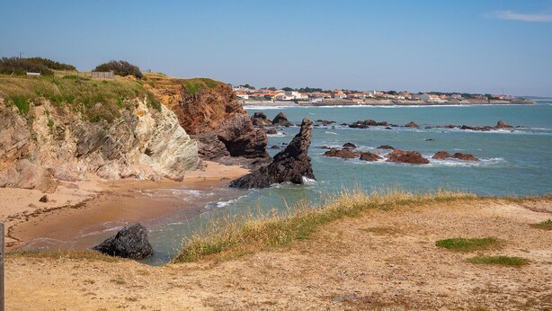 Paisaje costero con acantilados rocosos, una playa arenosa y una vista distante de casas.