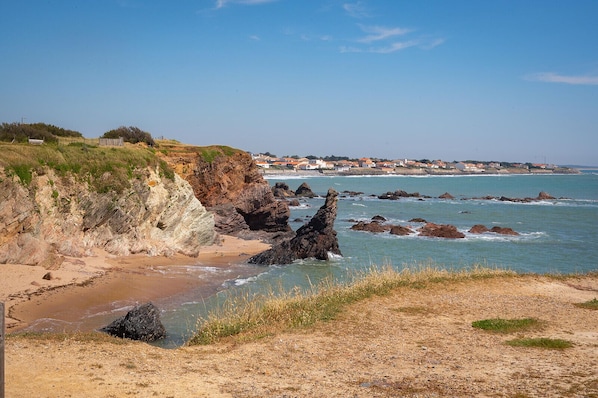 A coastal landscape with rocky cliffs, a sandy beach, and a distant view of houses. - Bois Marin - Pool & Beach 500 meters away (Bretignolles-sur-Mer)
