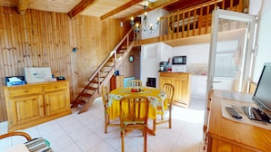 Interior de madera con una mesa de comedor, sillas, una escalera, zona de cocina y un televisor.