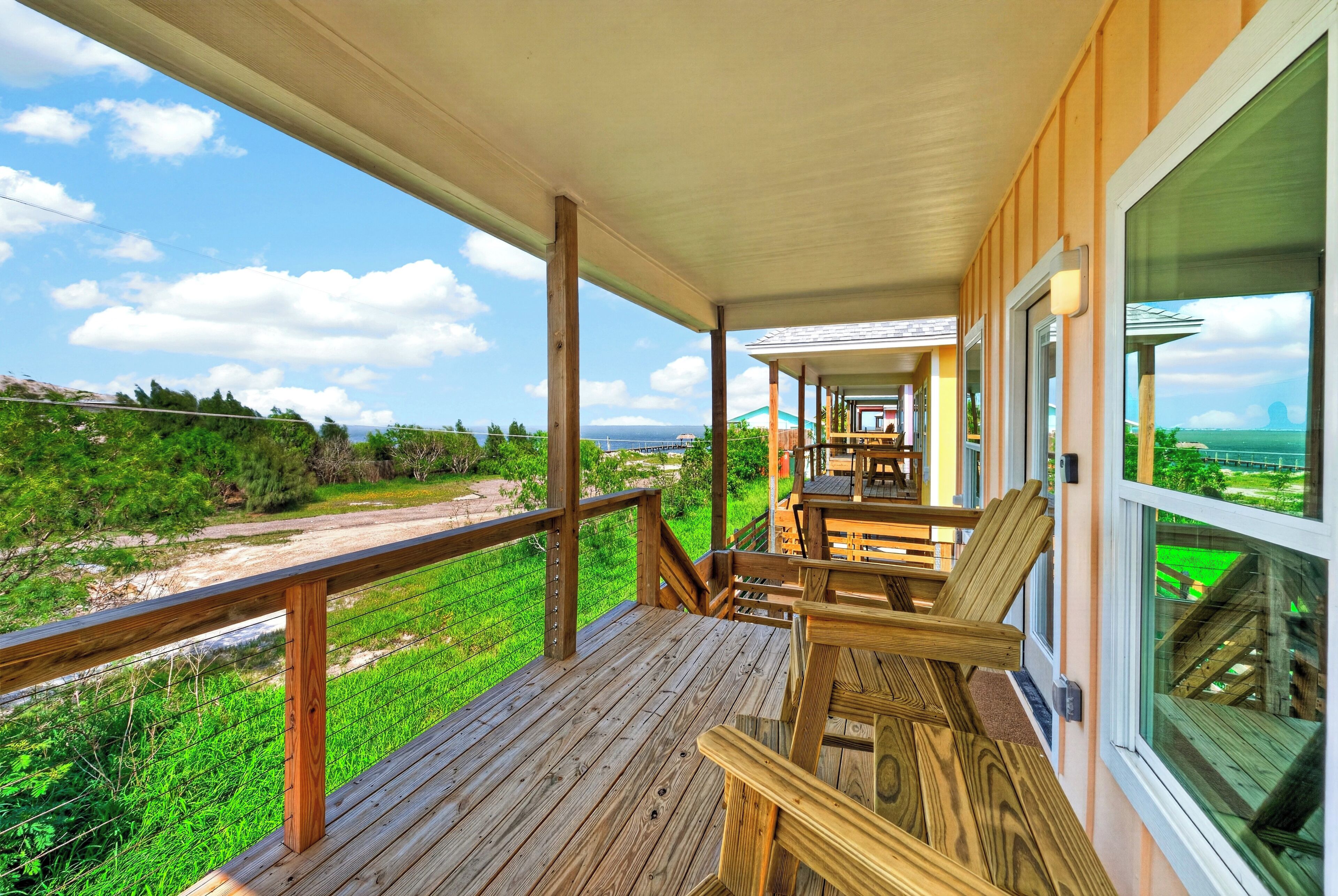 Une terrasse en bois, dotée d’une balustrade, qui donne sur une pelouse et offre une vue sur l’océan.