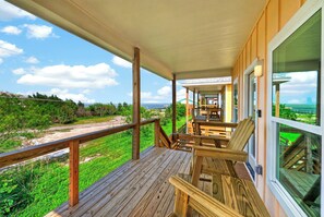 Eine Holzterrasse mit Geländer, die auf eine Wiese und den Blick aufs Meer blickt.