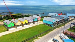 A coastal area with colorful houses, a pier, and a road. - Water Views | Wraparound Decks | Pool Access | Flour Bluff Bay | Black Drum (Corpus Christi)