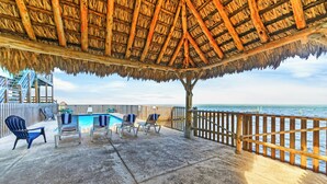 A covered outdoor area with a pool, lounge chairs, and a wooden railing overlooking the sea. - Water Views | Wraparound Decks | Pool Access | Flour Bluff Bay | Black Drum (Corpus Christi)