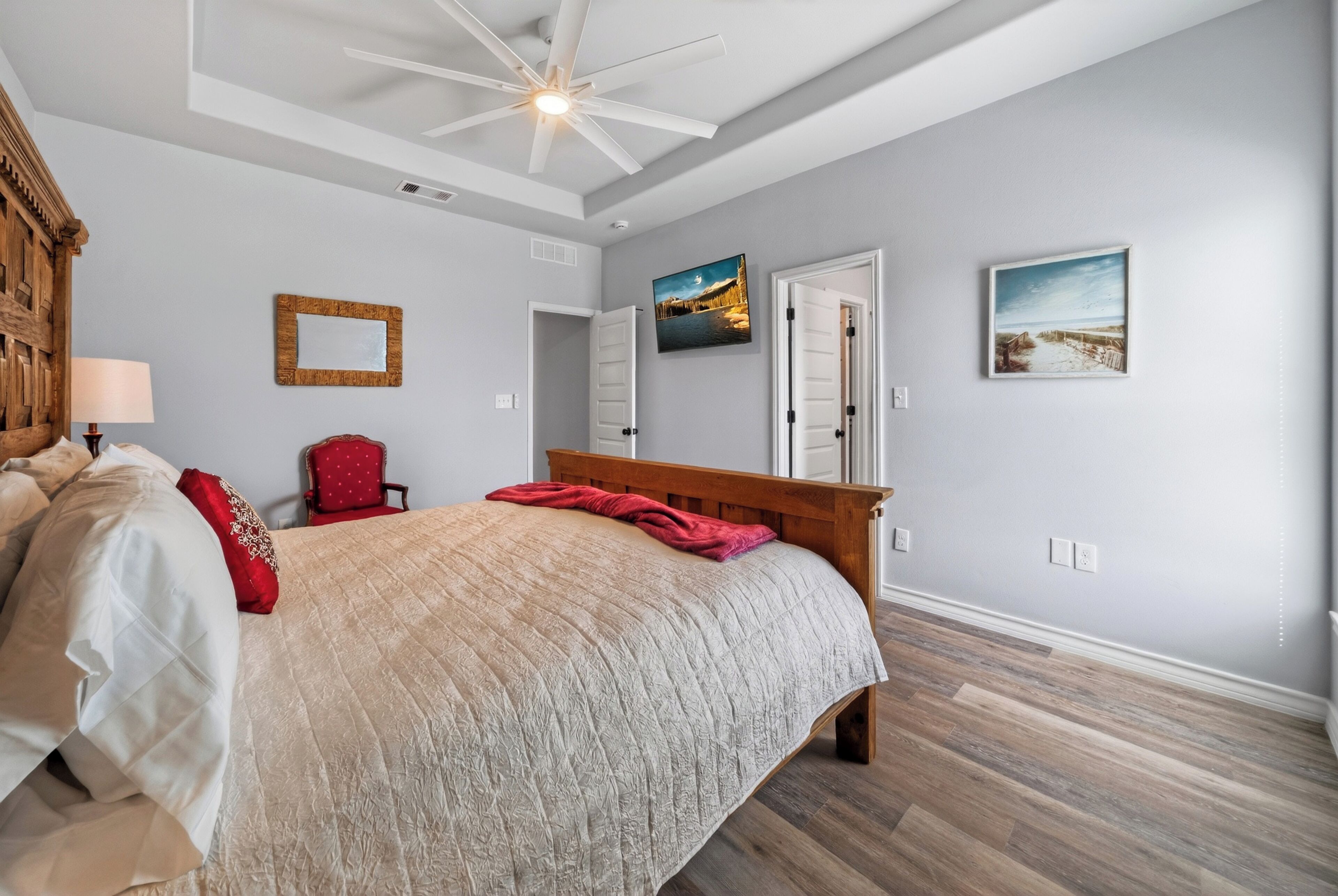 A bedroom with a bed, a wooden headboard, a ceiling fan, and a door.