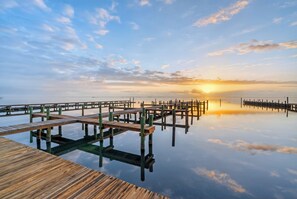 Eine Holzstege, der sich in ruhiges Wasser erstreckt, mit einem Sonnenuntergang im Hintergrund.