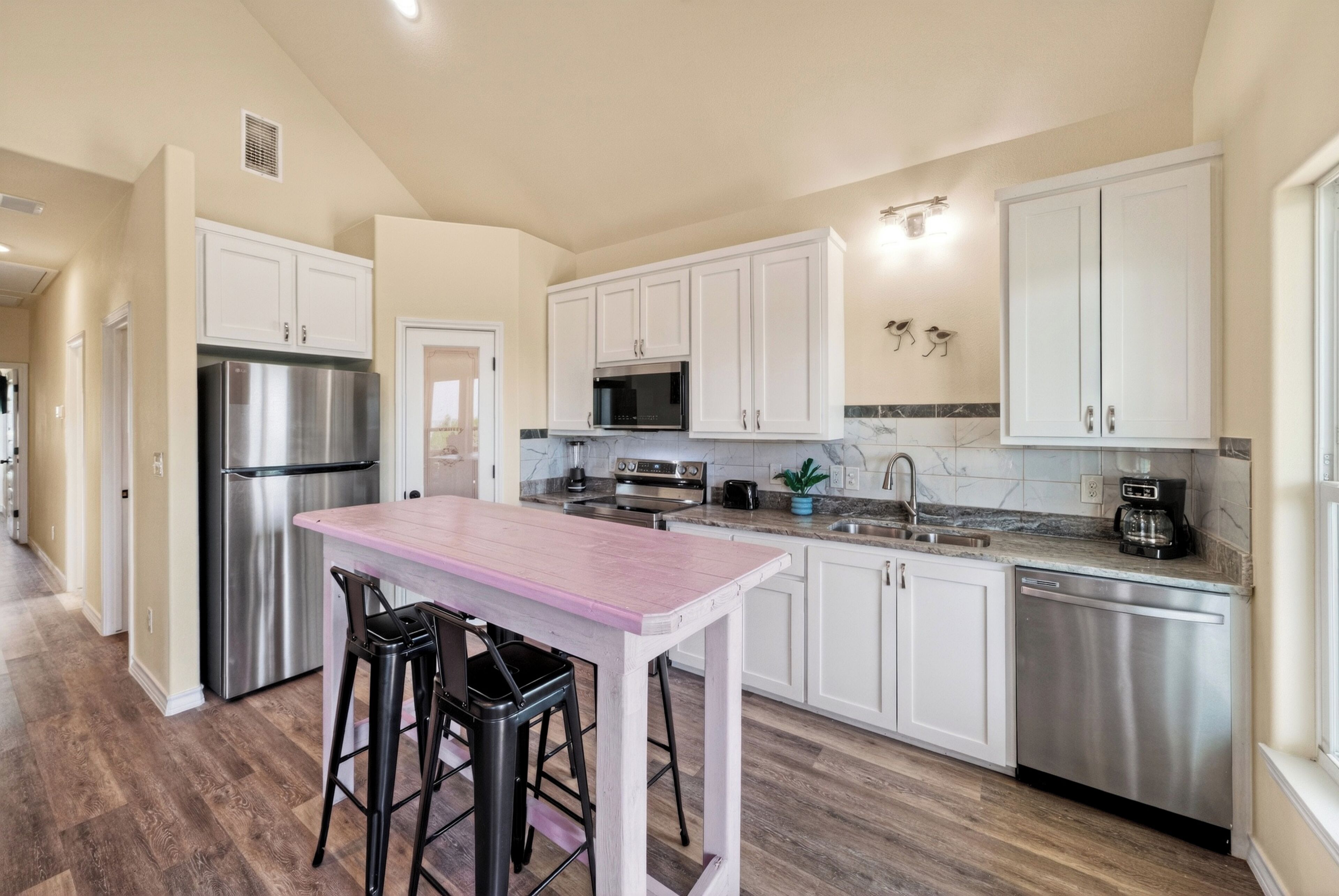 A modern kitchen with white cabinets, stainless steel appliances, and a wooden bar area.