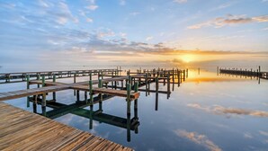 Een houten steiger die zich uitstrekt over kalm water, met een zonsondergang op de achtergrond.