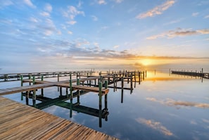 A wooden pier extending into calm water with a sunset in the background. - Bayfront  Home + Balcony | Shared Pool + Pier | Padre Island | Andy's Village (Corpus Christi)