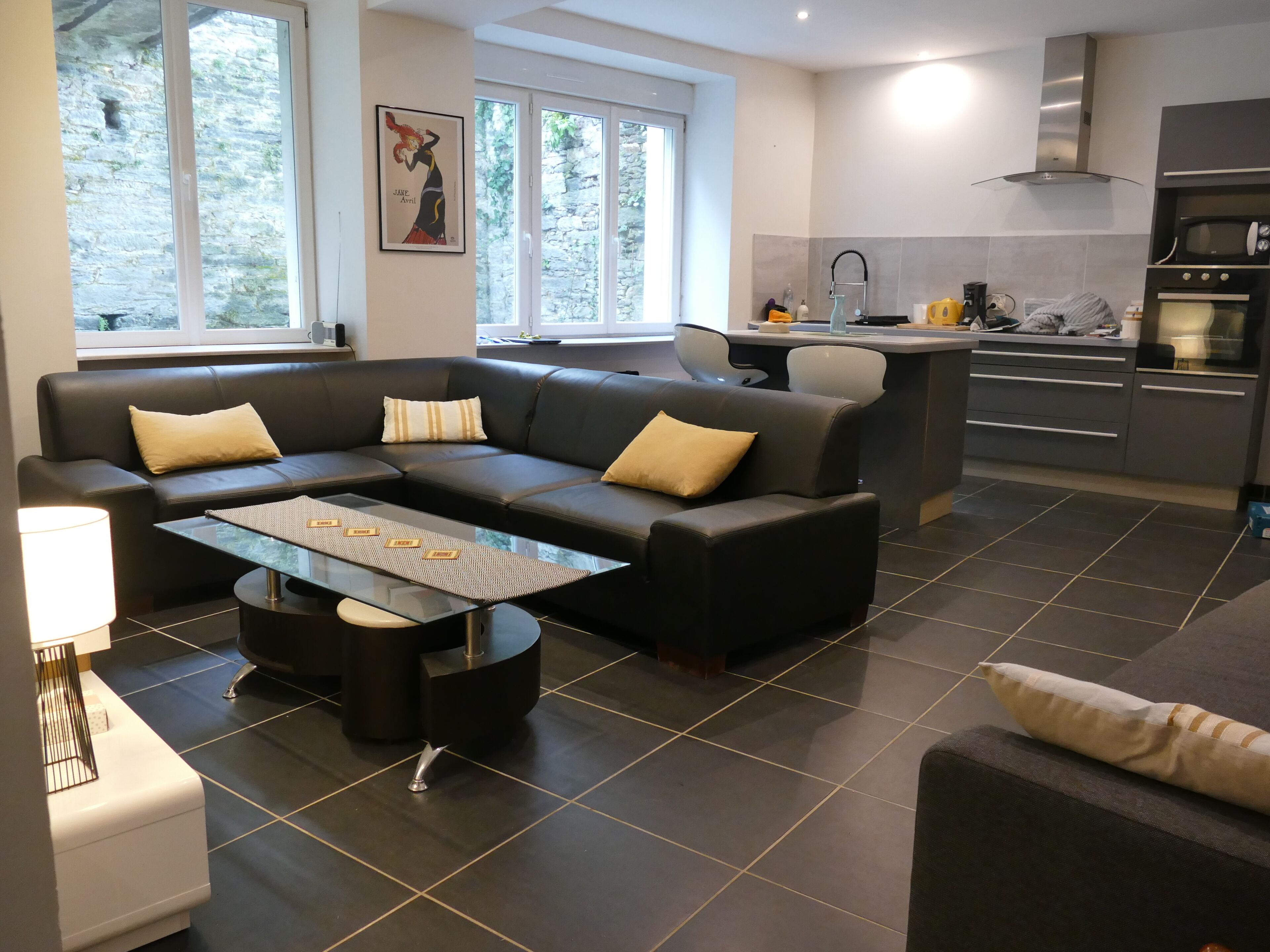 Un salon moderne comprenant un canapé, une table basse et un coin cuisine équipé d’appareils électroménagers.