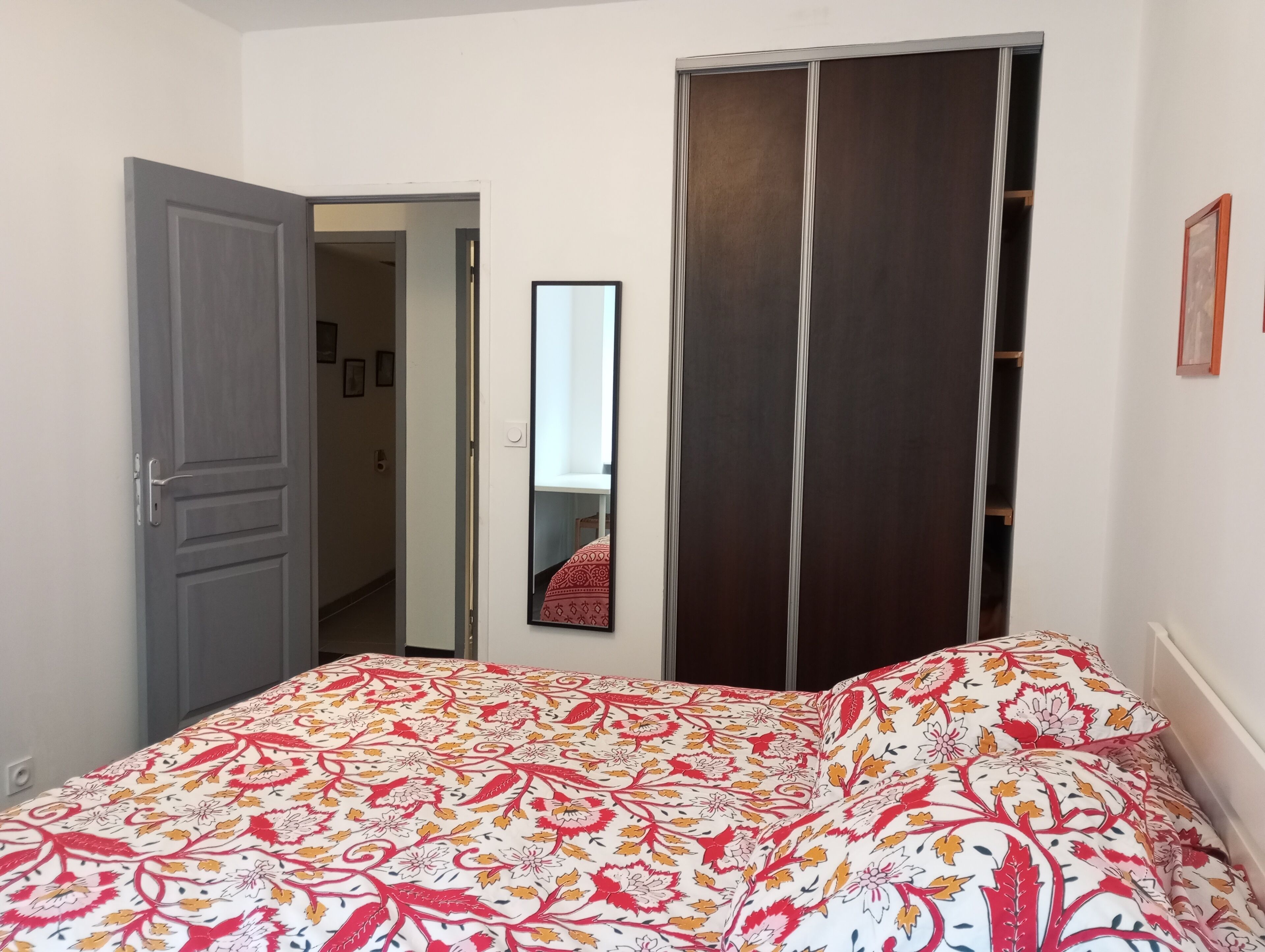 Une chambre à coucher comprenant un lit, une armoire, un miroir et une porte donnant sur une autre pièce.