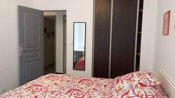 Une chambre à coucher comprenant un lit, une armoire, un miroir et une porte donnant sur une autre pièce.