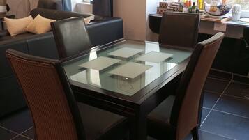 Een eethoek met een tafel met glazen blad, donkere stoelen, een bank en een wandklok.