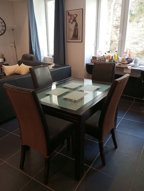Un coin repas comprenant une table à plateau en verre, des chaises foncées, un canapé et une horloge murale.