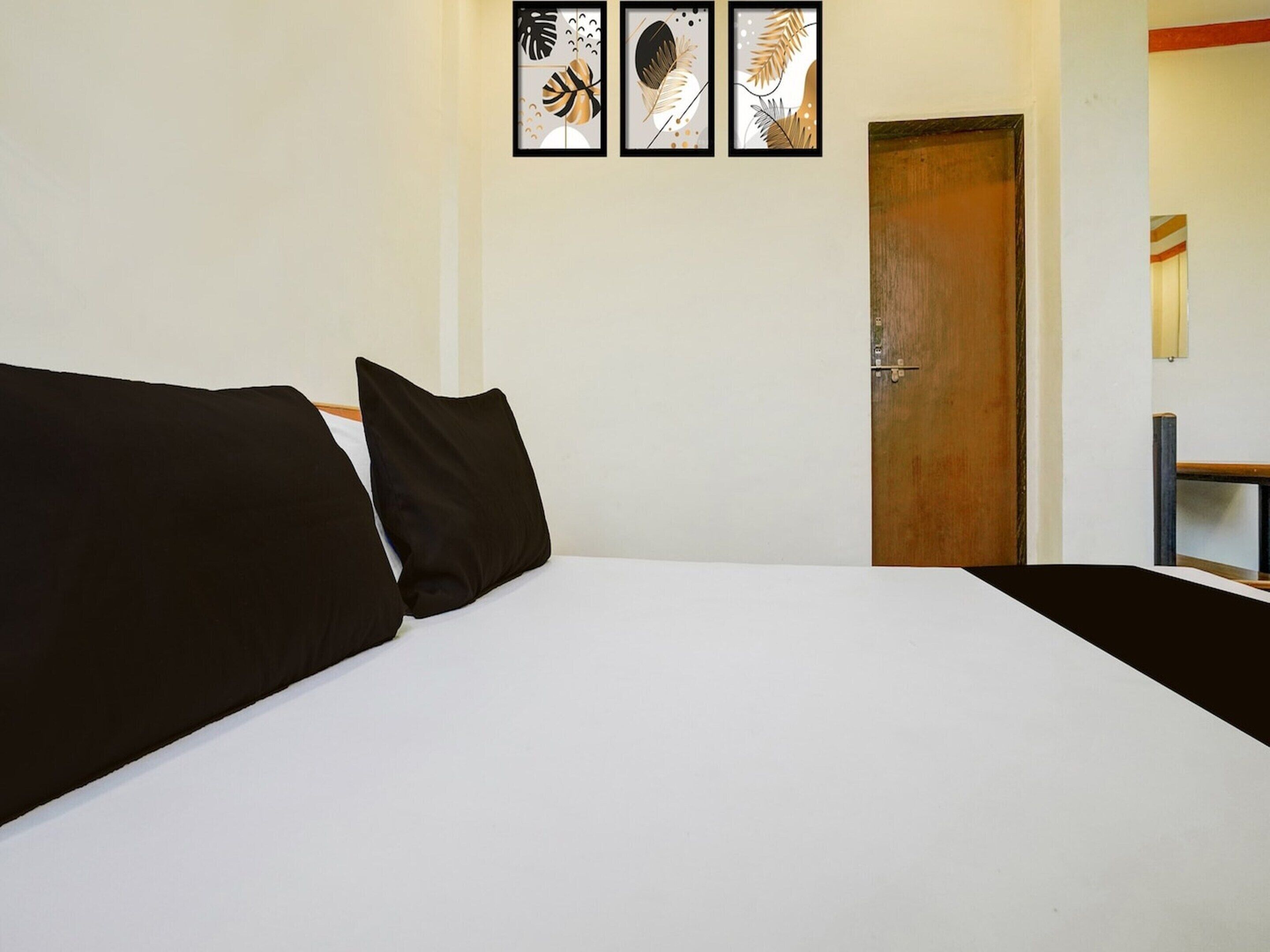 Een bed met zwart-wit beddengoed, een houten deur en drie ingelijste kunstwerken aan de muur.
