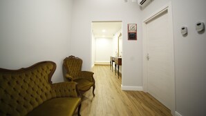 A hallway with a yellow upholstered sofa, a wooden chair, a white door, and an air conditioning unit. - Al Quadrato d'Oro (Catania)