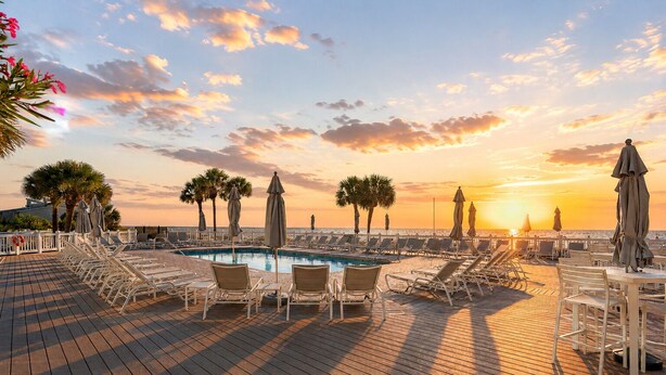 A poolside area with lounge chairs and umbrellas, a wooden deck, and a sunset view. - Steps to the Beach + Resort Pools + Golf | Wild Dunes IOP | 137 Grand Pavilion (Isle Of Palms)