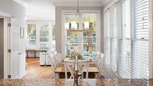 A dining area with a wooden table, white chairs, and a chandelier. - Steps to the Beach + Resort Pools + Golf | Wild Dunes IOP | 137 Grand Pavilion (Isle Of Palms)