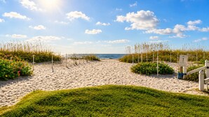 A sandy beach with a clear sky, a pathway leading to the sea, and a sign indicating a beach access point. - Steps to the Beach + Resort Pools + Golf | Wild Dunes IOP | 137 Grand Pavilion (Isle Of Palms)
