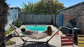Um quintal com piscina, rede, churrasqueira e deck de madeira.