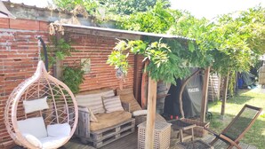 Um deck de madeira com uma cadeira suspensa, um banco estofado e uma mesa pequena.