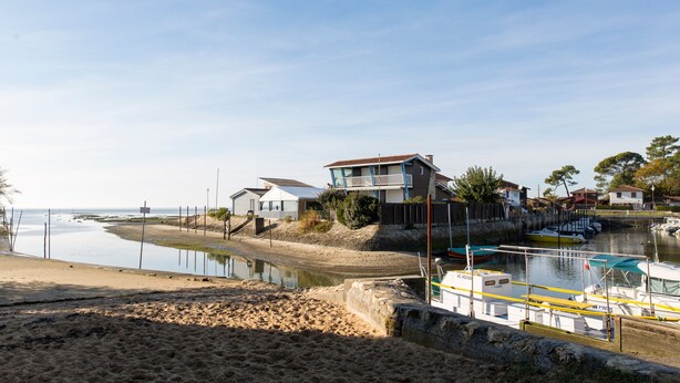 Uma propriedade costeira com praia, um cais com barcos e uma casa com varanda com vista para a água.