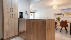 A modern kitchen with wooden cabinets, a coffee maker, and a dining area with a table and chairs. - Chateau Nouvella with balcony by Interhome (Blankenberge)