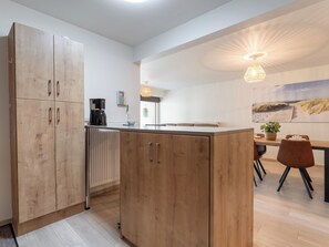 Eine moderne Küche mit Holzschränken, einer Kaffeemaschine und einem Essbereich mit Tisch und Stühlen.