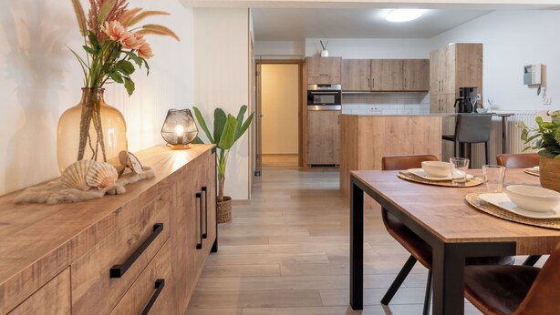 A modern kitchen with wooden cabinets, a dining table with chairs, and a vase with flowers on the counter. - Chateau Nouvella with balcony by Interhome (Blankenberge)