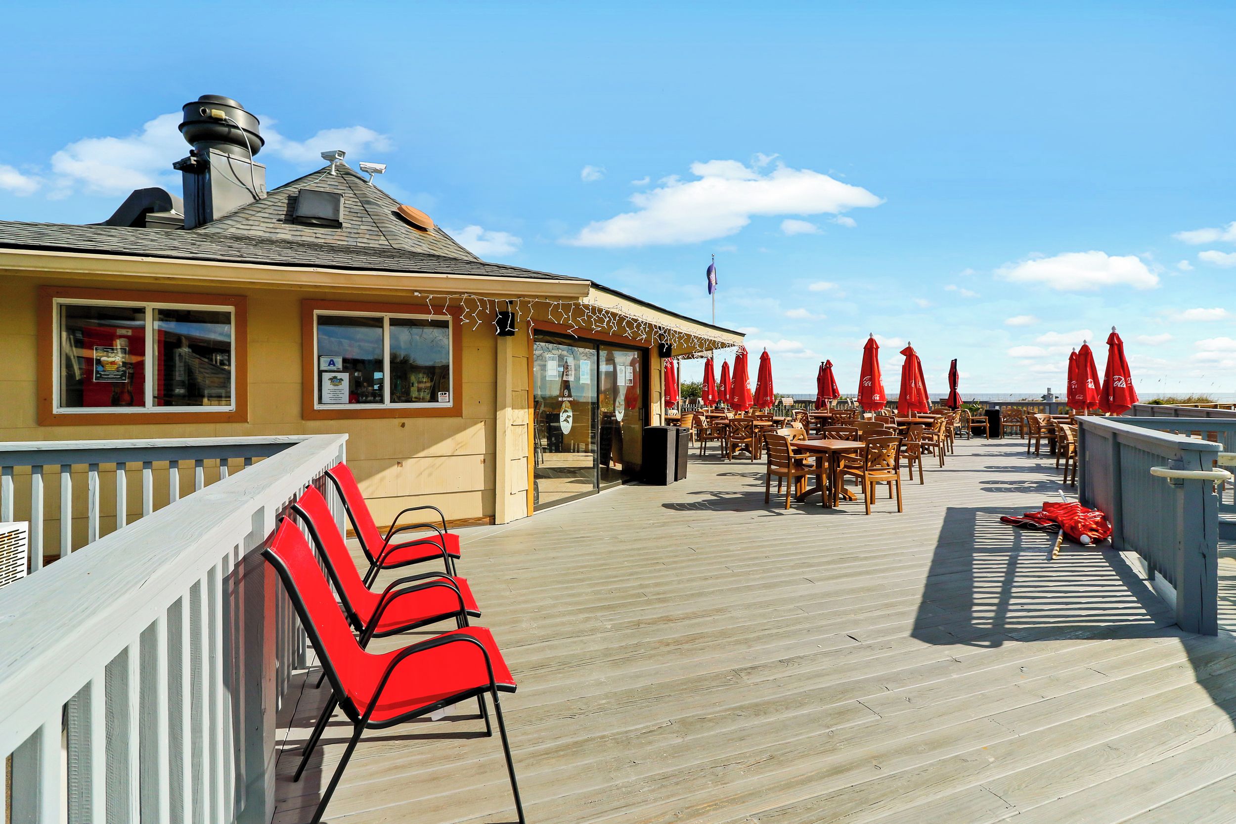 A deck with red chairs and tables, a building with a chimney, and a clear sky.