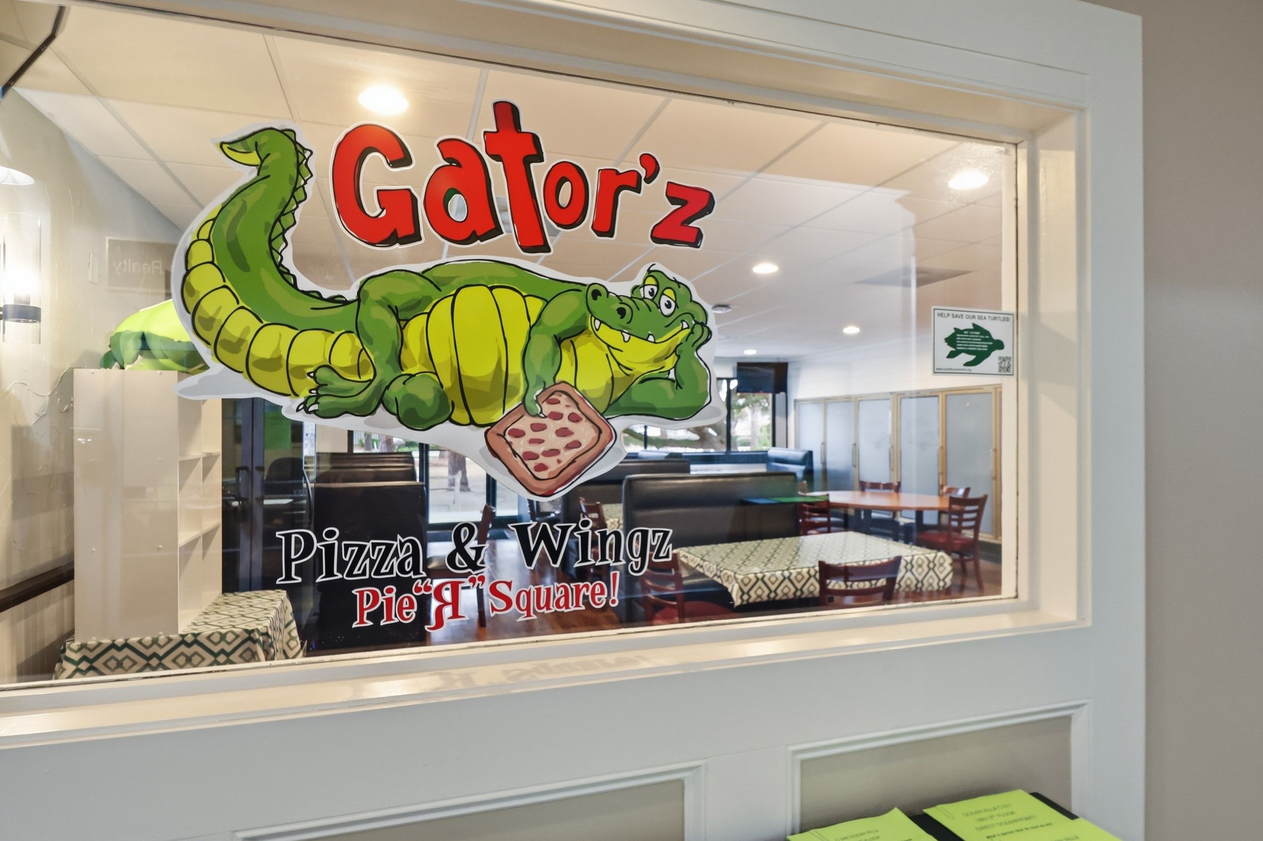 Une fenêtre de restaurant ornée d’un dessin de dinosaure et sur laquelle on peut lire le nom « Gatorz ».