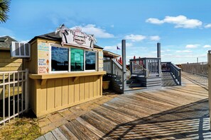 Ein hölzerner Eisstand mit Speisekarte, auf einer Holzpromenade mit einer Treppe, die zu einem Gebäude führt.