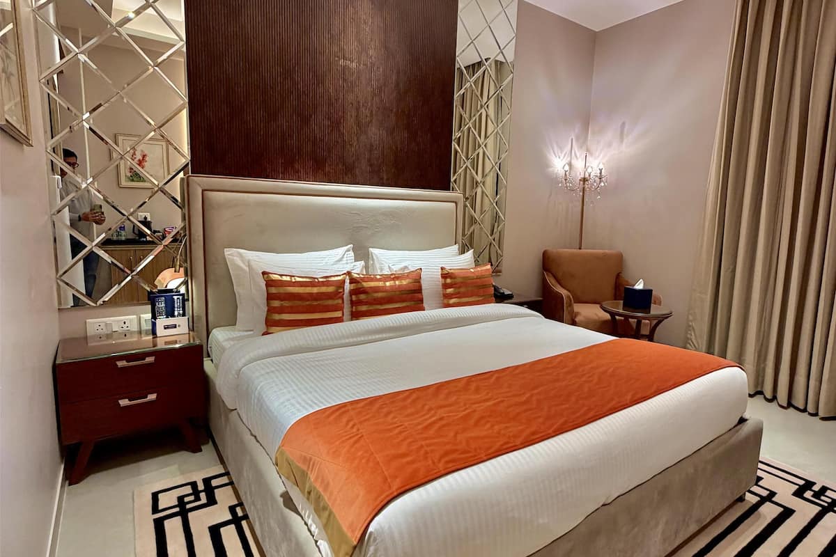 A modern hotel room with a large bed, a nightstand, a chair, a lamp, and a mirror.