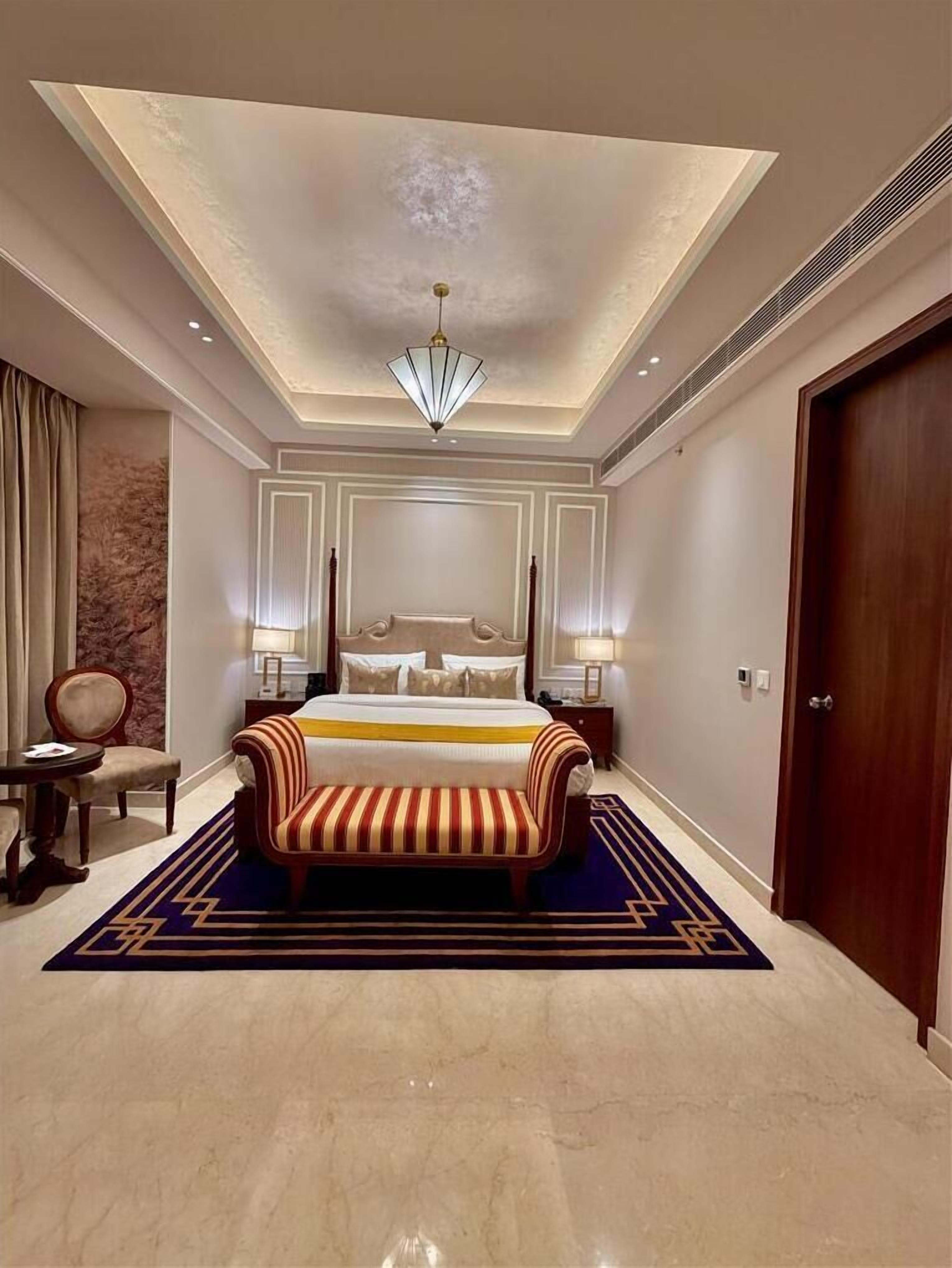 A hotel room with a large bed, a sofa, a chandelier, and a door.