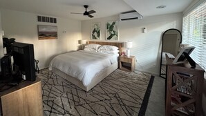 A bedroom with a bed, a ceiling fan, an air conditioning unit, a bedside table with a lamp, a mirror, and a TV on a stand. - Wine Country Cottage · King Bed · AC (Woodinville)