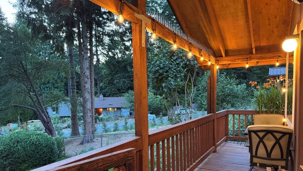 A wooden deck with a railing, a chair, and string lights.
