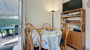Uma área de refeições com uma mesa, cadeiras, uma estante de livros e uma TV na parede.