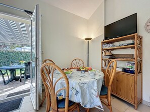 A dining area with a table, chairs, a bookshelf, and a TV on the wall. - Le Domaine du Golf by Interhome (Pornic)