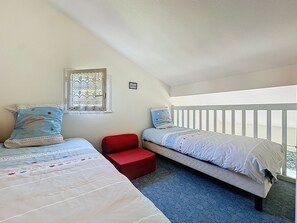 A bedroom with two beds, a red chair, a window with patterned curtains, and a white railing. - Le Domaine du Golf by Interhome (Pornic)