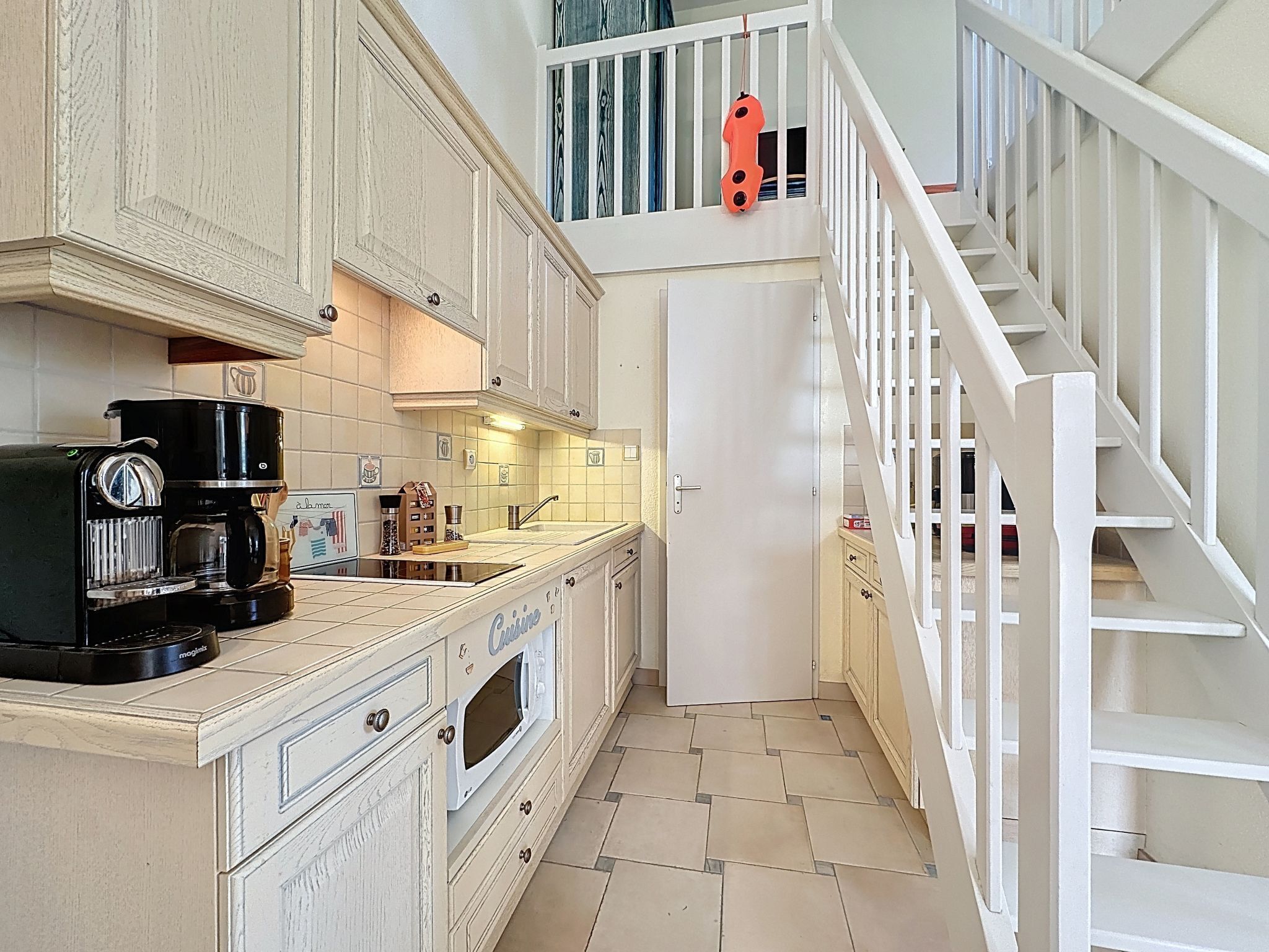 A compact kitchen with a coffee machine, a microwave, and a white staircase.